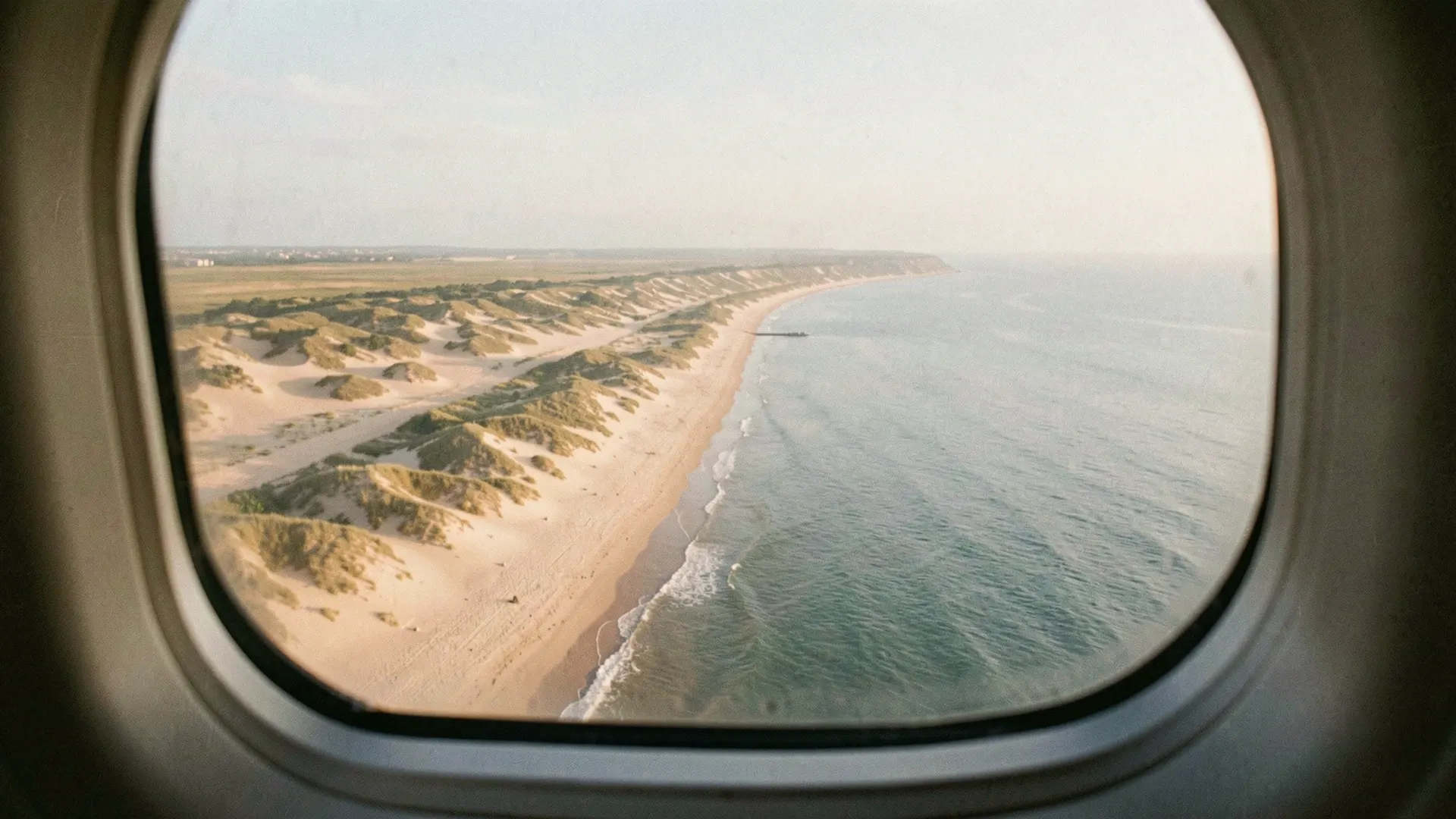 Illustration of dunes and an ocean beach seen through an airplane window
