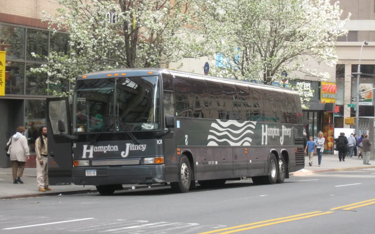 A dark Hampton Jitney coach parked at a Manhattan curb under flowering trees