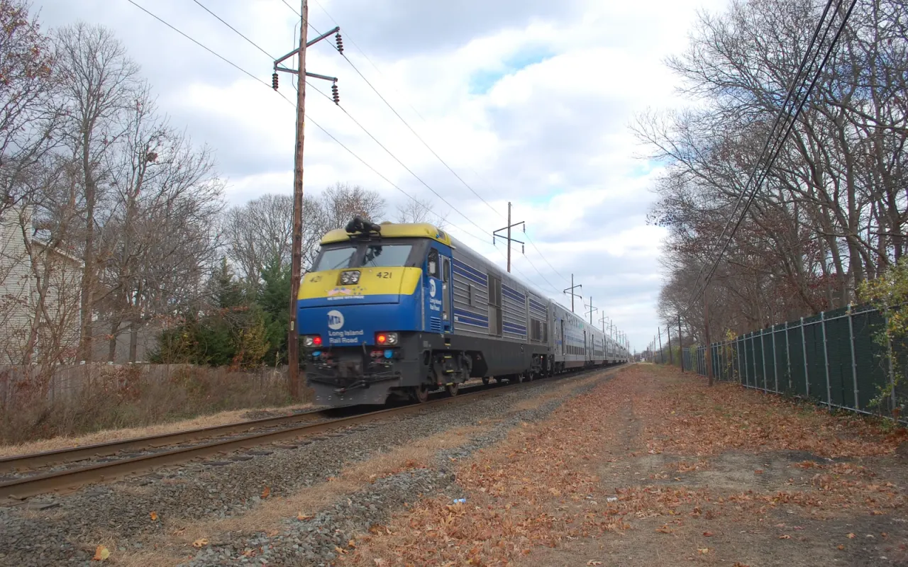 An LIRR diesel locomotive pulling double-decker cars past late-fall woods near Bayport on the Montauk Branch
